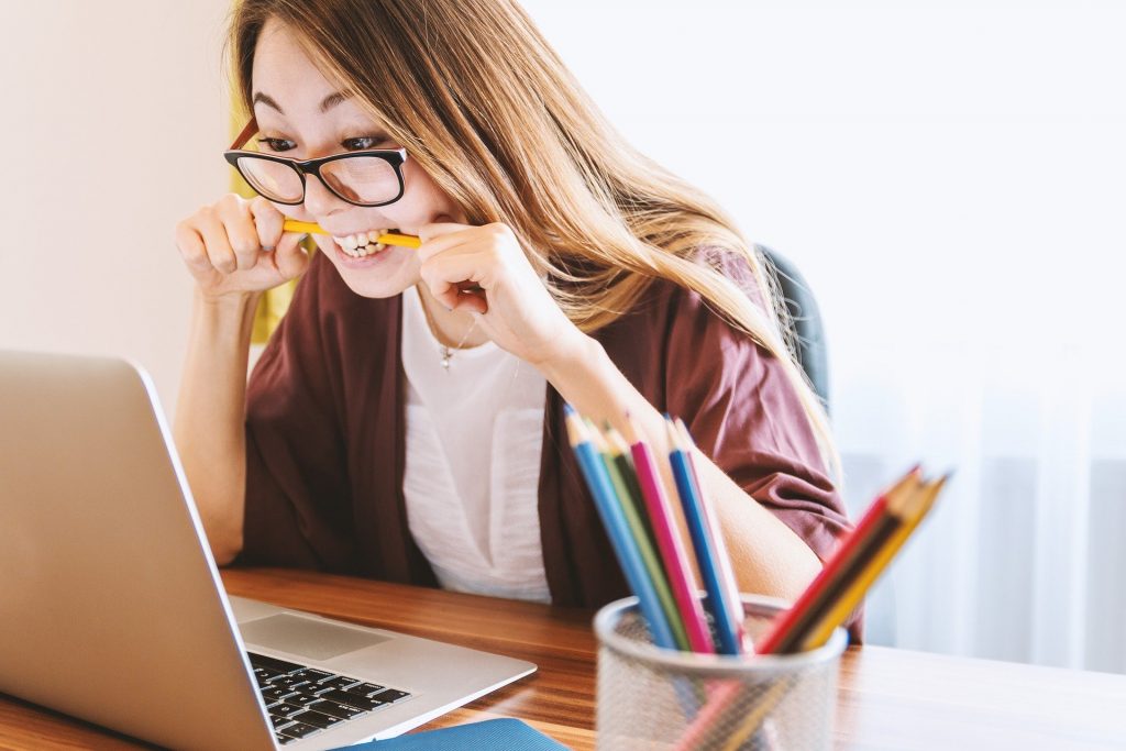 Female leader biting pencil while looking at laptop
